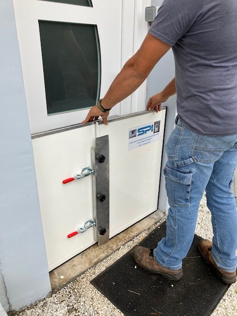 Un installateur insère le second panneau du batardeau dans le premier, devant une porte d'entrée